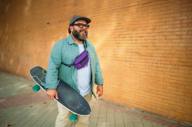 Dışarıda kaykay ve mor çanta taşıyan bir adam var..