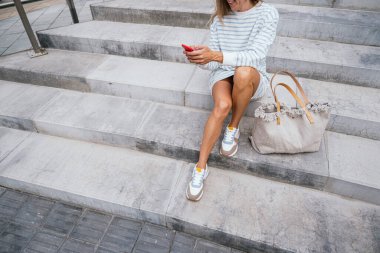 Merdivenlerde oturan bir kadın açık havada akıllı telefon kullanıyor..