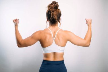 Kameraya arkası dönük duran, kaslarını ve kaslarını kasan bir kadın.