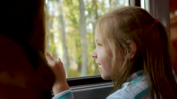 Симпатична маленька дівчинка посміхається і дивиться у вікно поїзда в кареті під час подорожі — стокове відео