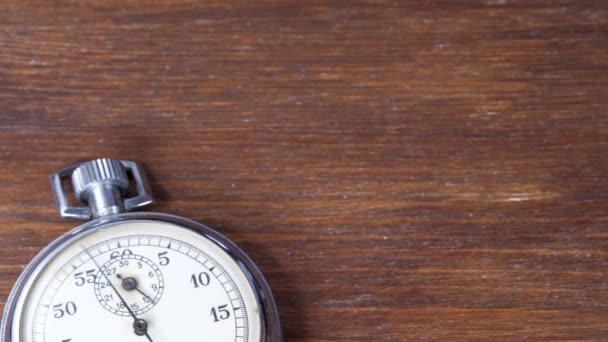 Analogue stopwatch hands counts down seconds on brown wooden background — Stock Video