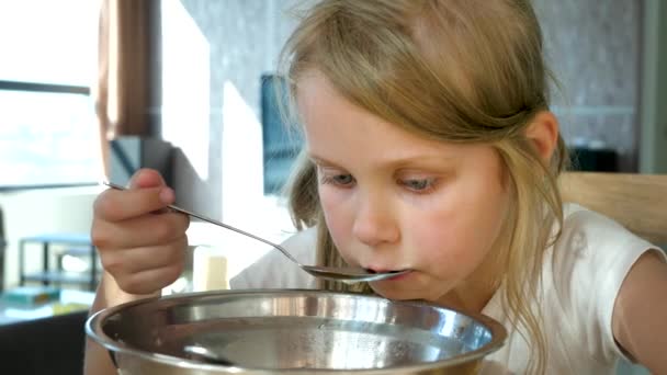Menina muito caucasiana com incríveis olhos azuis tomando sopa de macarrão da colher dentro de casa — Vídeo de Stock