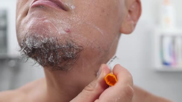 Pemuda tampan dengan busa di wajahnya bercukur menggunakan pisau cukur — Stok Video