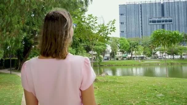 Bonito feminino olha para paisagem urbana com lagoa e fundo de árvores verdes — Vídeo de Stock