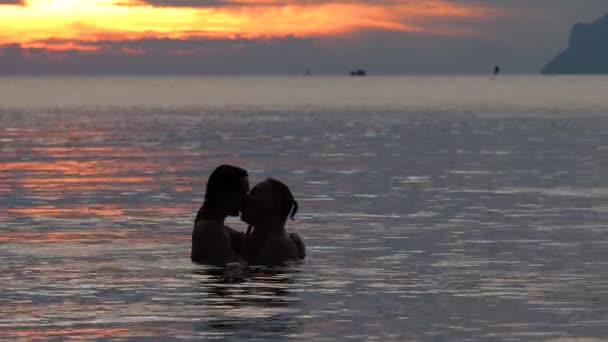 Щаслива пара плаває, обіймається і цілується у морській воді під час заходу сонця — стокове відео