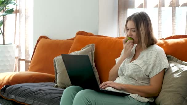 Carino creativo blogger donna digitando testo sul computer portatile e mangia mela verde a casa — Video Stock