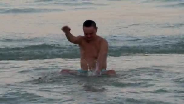 Смешной человек брызгает водой и купается в морской волне — стоковое видео