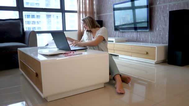 Jovem senhora atraente senta-se no chão, fala em Smartphone, trabalha horas extras com laptop e documentos — Vídeo de Stock