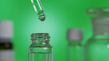 Cam şişedeki pipetten dökülen temiz bir damla organik esans yağı.