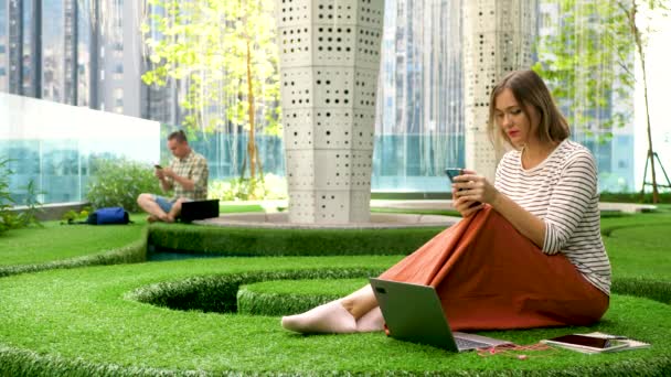 女性のかわいいオフィスワーカーは緑のコワーキングスペースでスマートフォンを使用します — ストック動画