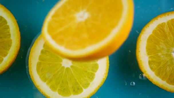 Φρέσκα φρούτα πορτοκάλι φέτα πέσει κάτω στην επιφάνεια του νερού σε μπλε πράσινο φόντο — Αρχείο Βίντεο