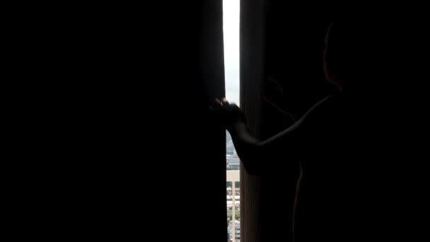 Чоловік відкриває темну завісу вікна вранці — стокове відео