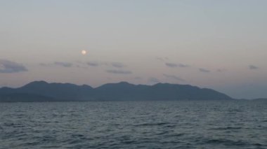 Suyun üzerindeki gemiden, dolunaydan ve karadaki dağların ana hatlarından görüntü 
