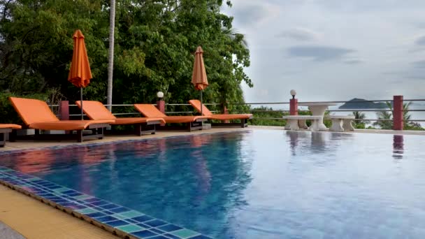 Пляжний стілець і помаранчева парасолька біля басейну з віллами на курорті — стокове відео