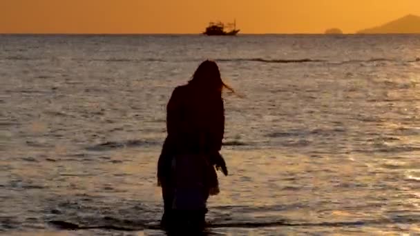 Las siluetas de la madre y la hija caminan sobre la superficie del agua de mar en la puesta de sol dramática — Vídeo de stock