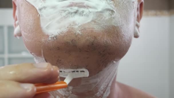 Pria tak dikenal mencukur busa di wajah menggunakan pisau cukur warna oranye — Stok Video