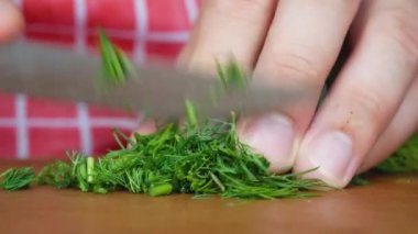 Ahşap mutfak tahtasının üzerinde bıçakla doğranmış dereotu.