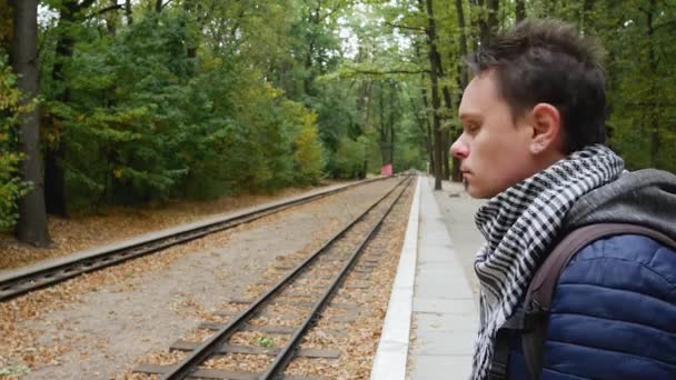 Jonge man wacht op trein op schort en kijkt naar horloge controleren tijd — Stockvideo