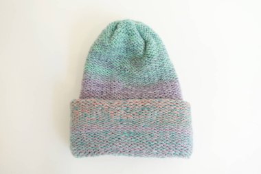 Cozy handmade beanie in soft pastel shades of mint, lavender, and peach, crafted from warm wool yarn and laid flat on a white surface.