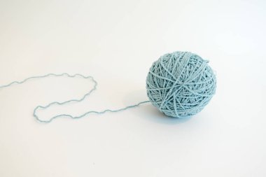 A soft light blue ball of yarn with a loose strand, placed on a clean white surface, representing creativity, craft, and simplicity.