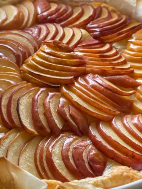 Tereyağlı bir kabuğun üzerinde ince dilimlenmiş kırmızı elmalar bulunan ve altın mükemmelliğinde pişirilmeye hazır güzel bir elmalı turtanın yakın çekimi..