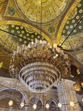 Karmaşık dekore edilmiş yeşil ve altın arabesklerle süslenmiş görkemli bir kristal avize İslami mimarinin ve kutsal iç güzelliğin çarpıcı bir örneği..