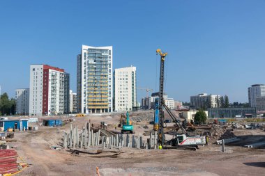 Espoo, Finlandiya - 1 Ağustos 2025: Finnoo 'daki Meritie karayolu şantiyesi, ağır ekipmanlar ve modern altyapı gelişiminin ortasında yere beton yığınları döşeyen güçlü bir kazık makinesi