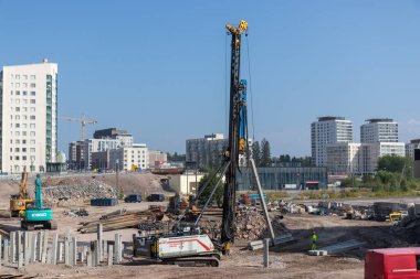 Espoo, Finlandiya - 1 Ağustos 2025: Finnoo 'daki Meritie karayolu şantiyesi, ağır ekipmanlar ve modern altyapı gelişiminin ortasında yere beton yığınları döşeyen güçlü bir kazık makinesi