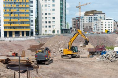 Kazıcıların ve kamyonun büyük toprak yığınları arasında faaliyet gösterdiği, yeni bir yol ve kentsel altyapı için zemin hazırlayan bir yerleşim alanındaki inşaat alanı.