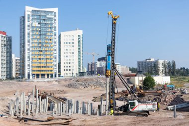 Güneşli bir günde, yerleşim alanındaki inşaat alanında ağır makinelerin yere beton yığınları yığdığı kentsel gelişim ve altyapı alanında ilerleme kaydedildiği bir gün.