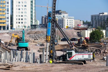 Güneşli bir günde, yerleşim alanındaki inşaat alanında ağır makinelerin yere beton yığınları yığdığı kentsel gelişim ve altyapı alanında ilerleme kaydedildiği bir gün.