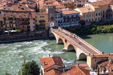 İtalya 'nın Verona kentinin hava manzarasında, Adige Nehri' ni geçen antik Ponte Pietra köprüsü, kırmızı kiremitli çatılar ve Veneto bölgesinin tarihi kalbiyle çevrilidir.