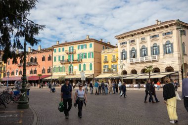 İtalya, Verona - 1 Ekim 2025: Verona 'daki canlı Piazza Sütyeni güneşli bir sonbahar gününde turistlerle dolu, renkli tarihi binalar ve eski şehir merkezinin sıcak cazibesi ile çevrili.