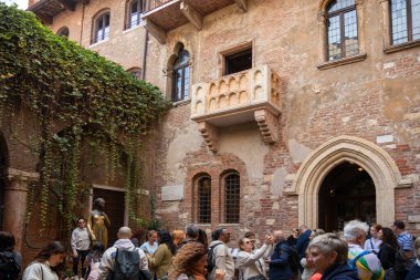 İtalya, Verona - 1 Ekim 2025: Turistler aşkın simgesi ve en romantik simgelerinden biri olan Casa di Giulietta 'nın balkonunun altındaki Juliet heykelinin yanında toplandı.