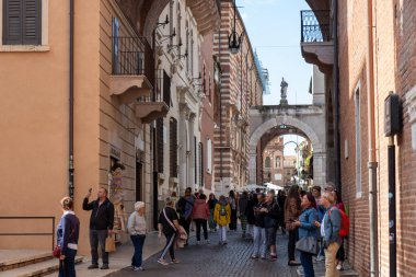 İtalya, Verona - 1 Ekim 2025: Dar bir sokaktaki turistler renkli eski binalar, balkonlar ve panjurlarla dolu, tarihi şehrin ve zamansız İtalyan atmosferinin cazibesini yakalıyorlar.