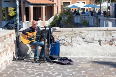 İtalya, Verona - 1 Ekim 2025: Bir İtalyan caddesinde gitar ve mikrofonlu sokak müzisyeni, havayı canlı müzikle dolduruyor ve yoldan geçenler için sıcak, canlı bir atmosfer yaratıyor.