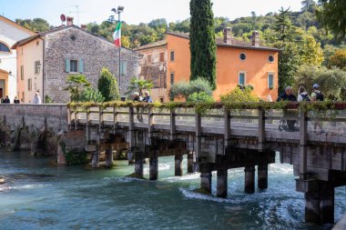 İtalya, Borghetto - 2 Ekim 2025: Turistler, nehir manzarası ve büyüleyici eski evleri ile tanınan ünlü bir turistik yer olan Borghetto ortaçağ köyündeki tarihi köprüyü ziyaret ettiler