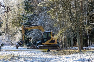 Bir kazıcı, kış koşulları ve sakin, donmuş bir manzarayla çevrili, karla kaplı bir inşaat sahasında boşta duruyor.