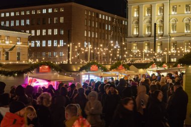 Helsinki, Finlandiya - 22 Aralık 2025: Helsinki Noel Pazarı Tuomaan Markkinat Senato Meydanı. Kutlama tezgahları, sıcak tatil ışıkları, Fin yemekleri, kafeler, turist ve ziyaretçi dolu el sanatları