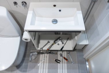 Musluk tamiri sırasında lavabo lavabo lavabosu, etrafta aletlerle. Ev yenileme sahnesi tesisat onarımı, bakım ve kurulum çalışmalarını gösteriyor
