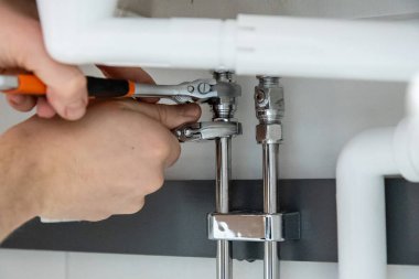 Tesisat işi yapan ellerin yakın çekimi, iki anahtarla boru tesisatını sıkılaştırmak. Güvenli bağlantılar ve düzgün bakım sağlanması için profesyonel kurulum veya onarım görevi