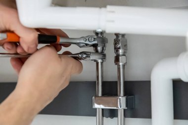Tesisat işi yapan ellerin yakın çekimi, iki anahtarla boru tesisatını sıkılaştırmak. Güvenli bağlantılar ve düzgün bakım sağlanması için profesyonel kurulum veya onarım görevi