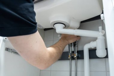 Tesisat işi yapan, boru tesisatını sıkan ellerin yakın çekimi. Güvenli bağlantılar ve düzgün bakım sağlanması için profesyonel kurulum veya onarım görevi