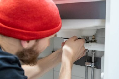 Tamirci, modern bir banyoda döşemeleri döşemeli banyo lavabosunun altına yeni bir musluk ve tesisat hattı kuruyor. Tamir, bakım ve uygun montaj çalışmalarını gösteren ev yenileme sahnesi