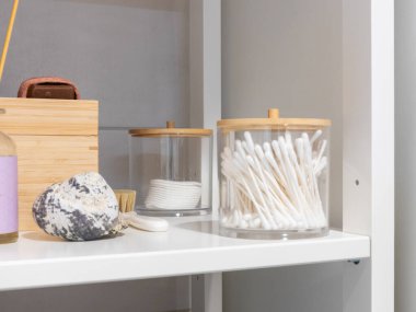Bambu kapaklı temiz akrilik saklama kavanozları bir banyo rafında, pamuklu bezler ve pamuklu pedleri tutarak düzenli, düzenli ve çevre dostu kişisel bakım düzeneği oluşturuyorlar.