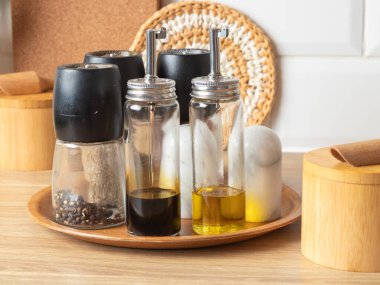 Yuvarlak bir bambu servis tepsisi tuz ve biber değirmenleri, bir yağ ve sirke şişesi ve bir kürdan kabı seti içerir, düzenli ve şık bir masa organizasyonu oluşturur.