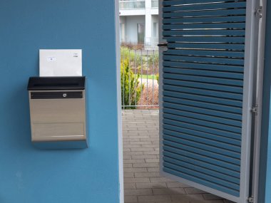 Modern, paslanmaz çelik duvar monteli bir posta kutusu. Siyah bir kapağı, gazete tutacağı, güvenli bir kilidi ve dayanıklı, havaya dayanıklı bir yapısı var.