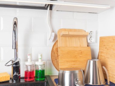 Temizlik malzemeleri, bambu kesme tahtaları ve metal kaplarla dolu temiz bir mutfak lavabosu. Organizasyon, hijyen, verimli ev işleri ve basit, modern bir ev düzeni öneriyor.