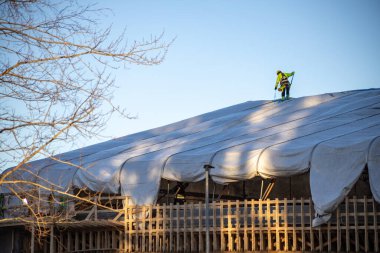 Espoo, Finlandiya - 12 Aralık 2025: Finnoo inşaat Meritie karayolundaki bir alanı kaplayan büyük beyaz bir geçici kumaş barınağının üzerinde güvenlik teçhizatı kullanan bir inşaat işçisi duruyor