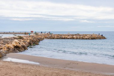 Kumlu bir sahil denize doğru kıvrılır ve uzun, kayalık bir dalgalanma suya doğru uzanır. Dalgakıran, balıkçılık ve yürüyüş, Guardamar, İspanya ve Akdeniz boyunca çok sayıda insan görülebilir.